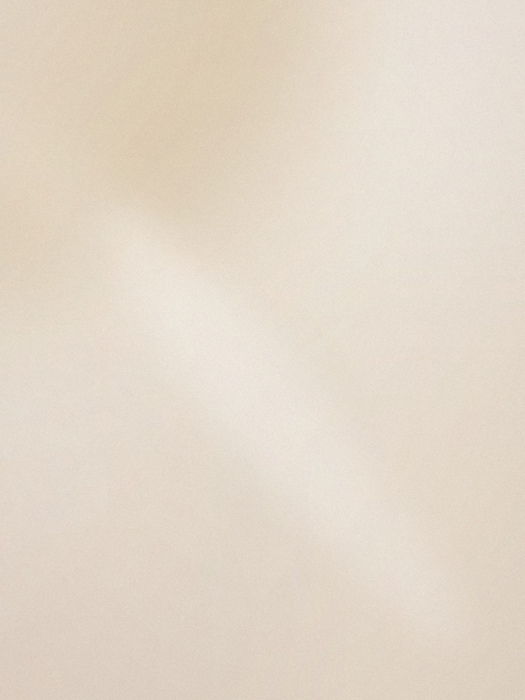 Volto con make-up leggero e luminoso, sguardo rivolto verso il basso su fondo neutro caldo